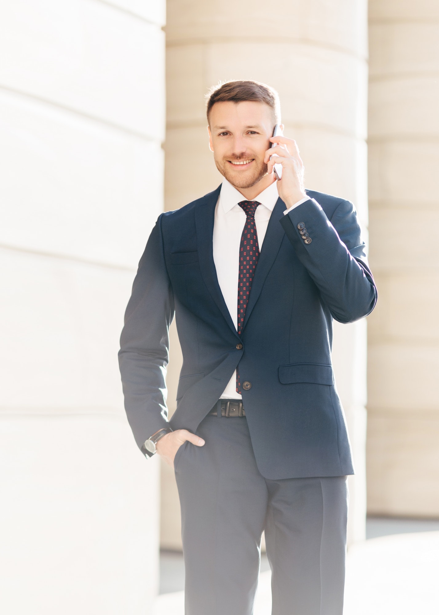 handsome successful male financial director solves problems via smart phone, looks confidently